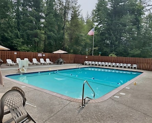 Ein Swimmingpool mit Holzterrasse, Liegestühlen und einer Flagge.