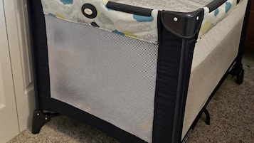 A portable crib with a mesh front and a handle, placed against a wall with a door and a lamp.
