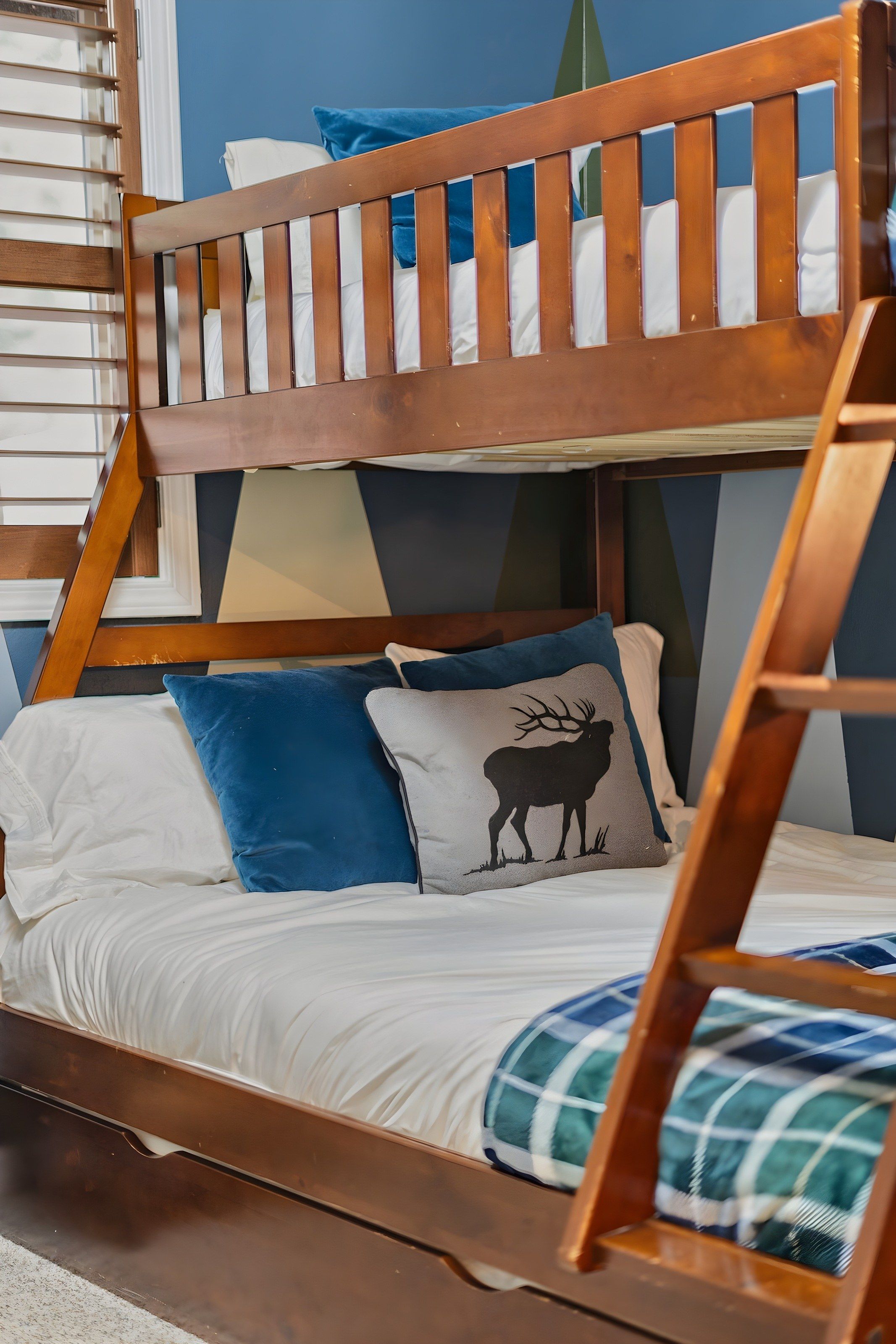 Un lit superposé avec une structure en bois, une literie blanche et un oreiller orné de la silhouette d’un cerf.