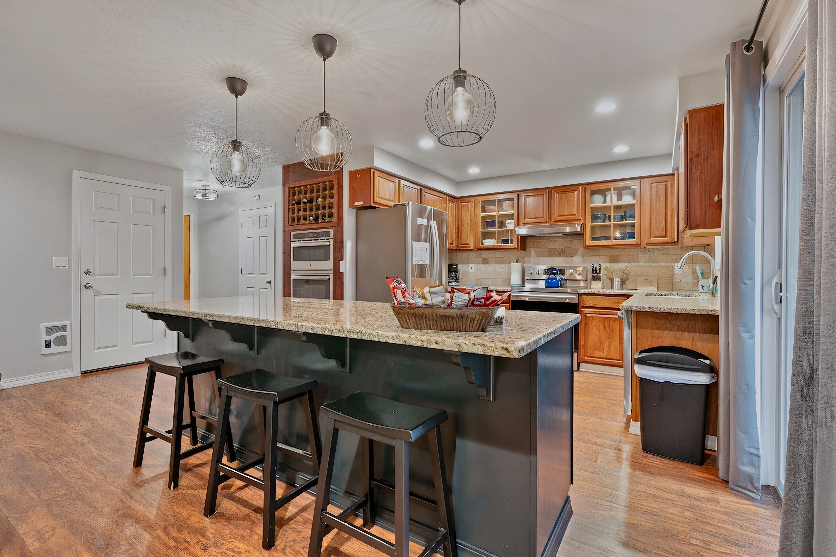 A modern kitchen with a central island, bar stools, wooden cabinets, and pendant lighting.