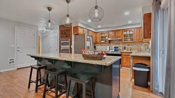 A modern kitchen with a central island, bar stools, wooden cabinets, and pendant lighting.