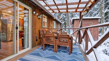 A wooden exterior with a covered patio area, a dining table with chairs, and a snow-covered landscape.