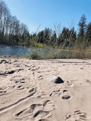 Ein sandiger Strand mit Fußspuren, einem kleinen Hügel und einem Fluss im Hintergrund.