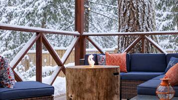 A wooden deck with a fire pit, blue cushioned seating, and a glass table.