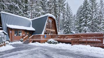A cabin with a sloped roof, wooden deck, and a snow-covered landscape.