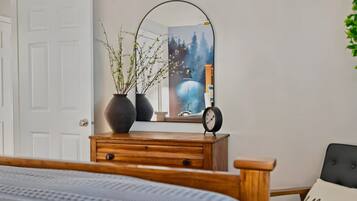 Ein Schlafzimmer mit einem Holzkoffer, einem Spiegel, einer Uhr und einem Bett mit grauem Kopfteil.