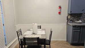 Un coin repas avec une table dressée pour quatre personnes, un luminaire au plafond et un espace cuisine avec des placards.
