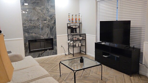 Un salon comprenant un canapé, une table basse en verre, un téléviseur, un ventilateur de plafond et un mur en marbre.