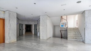 En rymlig hall med marmorgolv, en trädörr och en trappa med ett metallräcke.