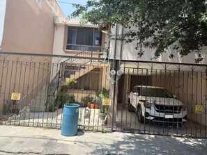 Un lotissement résidentiel fermé, avec une voiture blanche garée à l’intérieur, un baril bleu sur le trottoir et un escalier menant à un immeuble.