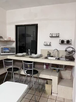 Une cuisine compacte équipée d’un four à micro-ondes, de deux tabourets de bar, d’un évier et d’une fenêtre.