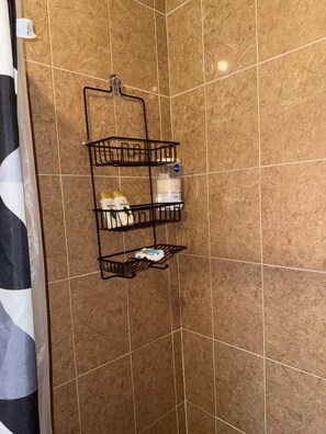 Une salle de bain avec une étagère d’angle où sont rangés les articles de toilette et un rideau de douche.