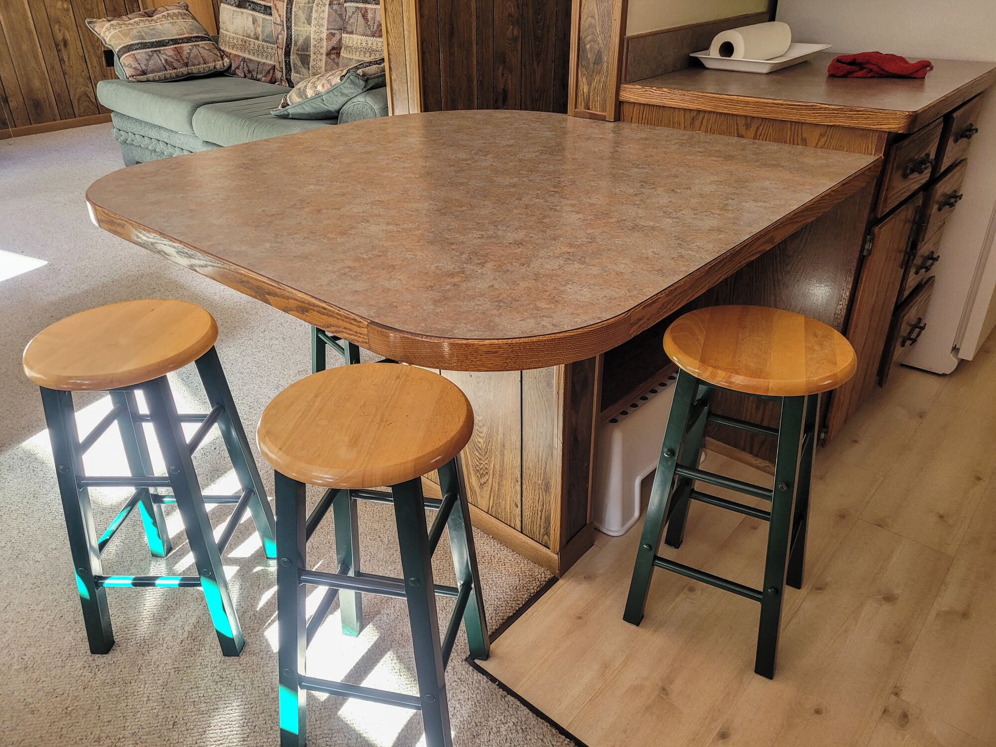 A kitchen with a large island, two stools, and a wooden cabinet.