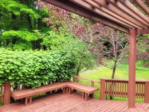A wooden deck with a bench, surrounded by lush green foliage and trees. - Peaceful retreat above the Delaware River (Pond Eddy)
