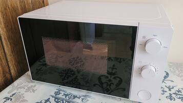 Un microondas blanco con interior negro, un panel de control con temporizador y ajustes de temperatura, y un mantel estampado debajo.