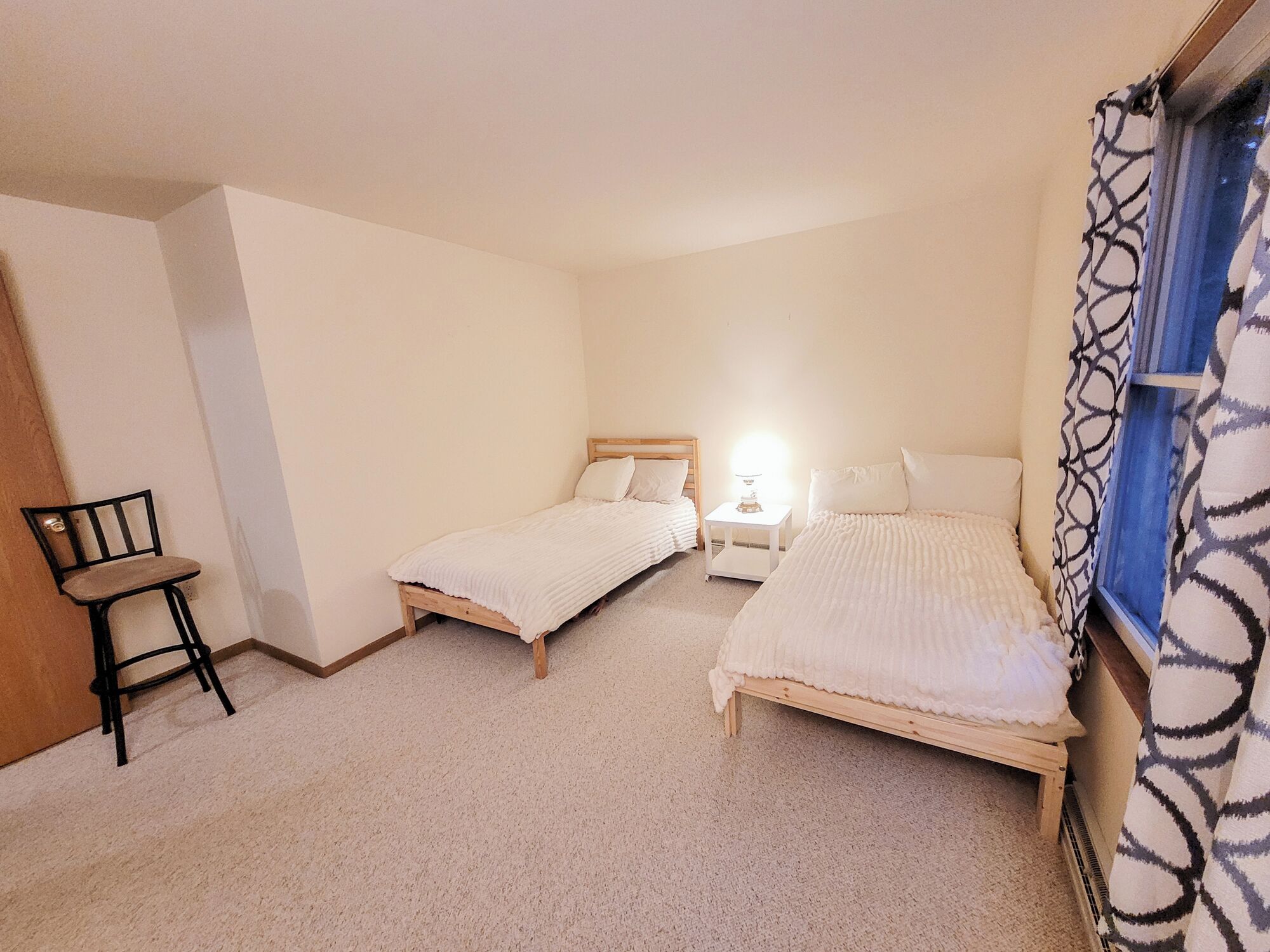 Een slaapkamer met twee bedden, een nachtkastje, een stoel en een raam met behang.