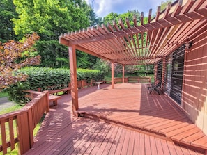 Une terrasse en bois agrémentée d’une pergola, de bancs et offrant une vue sur un bâtiment doté de grandes fenêtres.