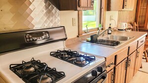 A kitchen with a gas stove, a sink, wooden cabinets, and a window. - Peaceful retreat above the Delaware River (Pond Eddy)