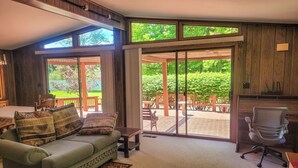 A cozy living room with a green sofa, a dining table, and a patio area with wooden furniture. - Peaceful retreat above the Delaware River (Pond Eddy)