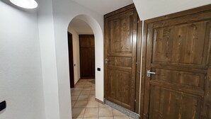 Un corridoio con pavimento piastrellato, pareti bianche e due porte in legno.