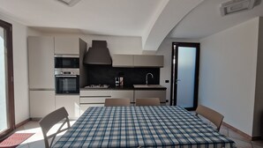 Angolo cottura compatto con microonde, forno e piano cottura a gas, tavolo da pranzo con sedie e vista all'esterno.