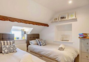 Ein Schlafzimmer mit zwei Betten, einem Oberlicht, einer Heizung, einem Regal mit gerahmten Bildern und einem kleinen Schrank.