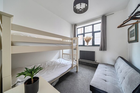 A bunk bed room with a radiator, a window with curtains, a plant, and a sofa.