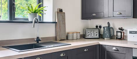 A modern kitchen with dark cabinetry, a stainless steel sink, a potted plant, a wooden cutting board, a toaster, a kettle, and a container labeled 'EGGS'.