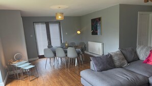 Uma sala de estar com sofá cinza, mesa de jantar com cadeiras, luminária pendente e radiador.