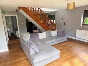 A living room with a grey sectional sofa, wooden staircase, and a hanging light fixture. - Cottage Sleeps 8 - Garden, Bbq, Pet-Friendly (Warwick)