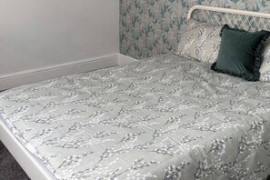 Ein Bett mit einem blumigen Überwurf, einem grünen Kopfkissen und einem Kopfteil.