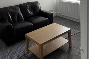Ein schwarzes Ledersofa und ein Holztisch in einem Raum mit einem gemusterten Teppich.