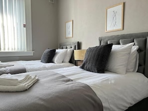 Ein Hotelzimmer mit zwei Betten, einem Fenster mit Jalousien und gerahmten Bildern an der Wand.