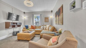 Ein modernes Wohnzimmer mit einer Sofagarnitur, einem Flachbildfernseher, einer Stehlampe und Kunstwerken an den Wänden.