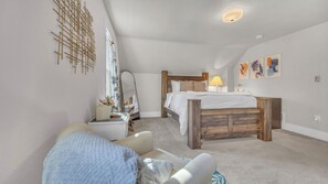 Une chambre à coucher avec un lit, une table de chevet, une lampe, un miroir et une œuvre d’art accrochée au mur.