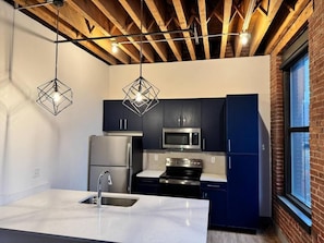 A modern kitchen with dark cabinets, stainless steel appliances, and geometric pendant lights. - Brick and Bed - City View Loft/Walk to Stadium, 301 (St. Louis)
