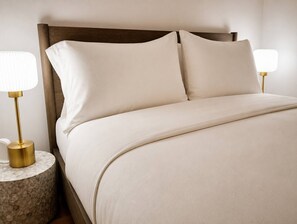 A bed with a wooden headboard, two bedside tables with lamps, and a plain wall. - Brick and Bed - City View Loft/Walk to Stadium, 301 (St. Louis)