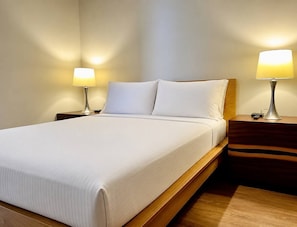 A neatly made bed with white linens, two bedside lamps, and a wooden nightstand. - Brick and Bed - City View Loft/Walk to Stadium, 301 (St. Louis)