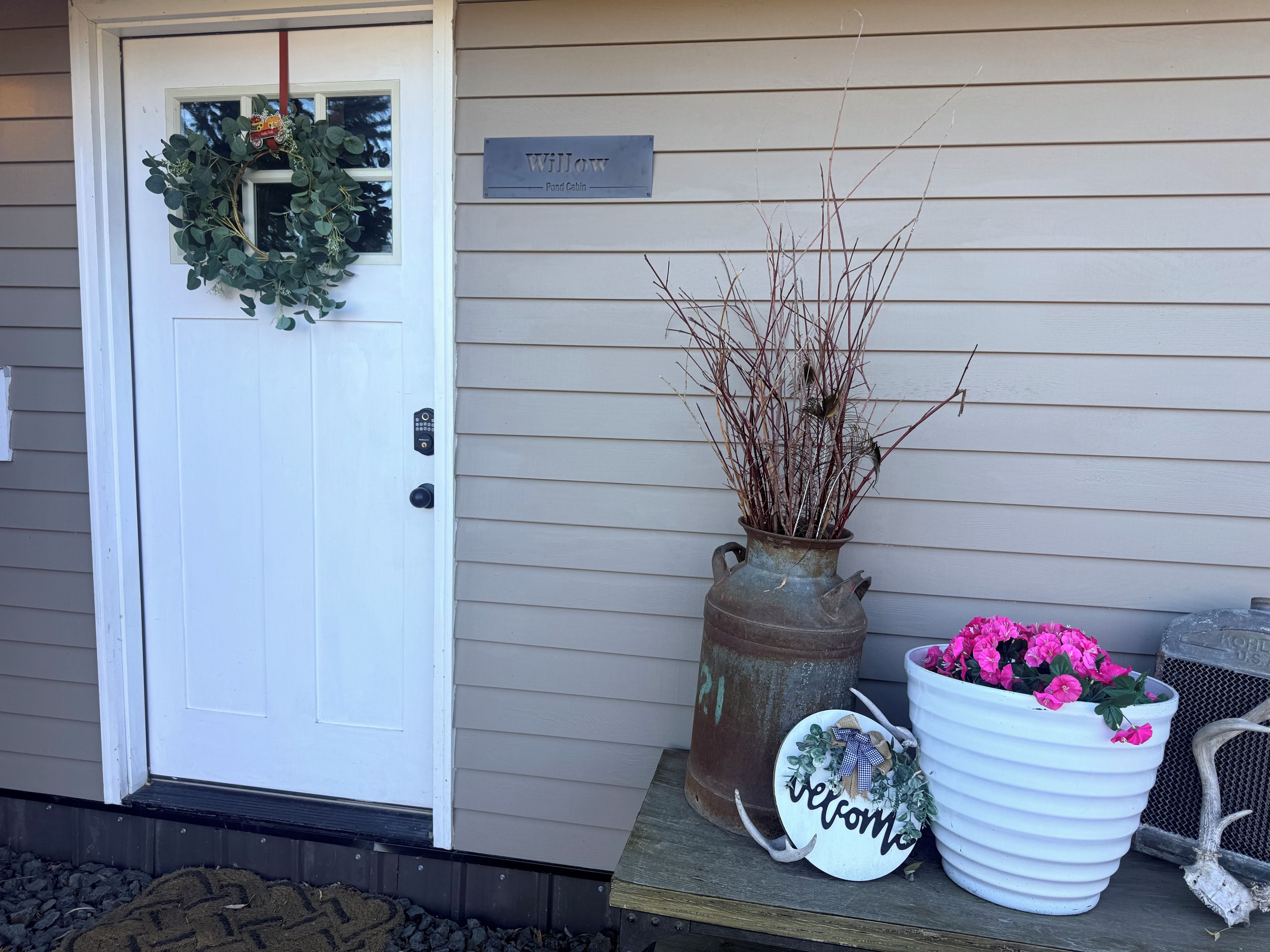 A front door with a wreath, a welcome sign, and two flower pots on a porch.