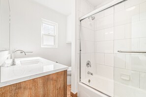 A bathroom with a white sink, a wooden vanity, a glass shower enclosure, and a window. - Walk 1/2 Block to the Beach from this Updated 4BR Coastal Home (Newport Beach)