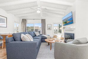 Ein Wohnzimmer mit Ecksofa, einem runden Couchtisch, einem Kamin und einem an der Wand montierten Fernseher.