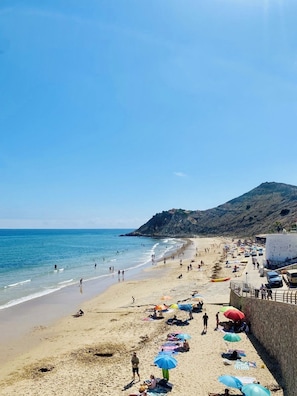 A beach with people, umbrellas, and a mountain in the background. - Luxury Apartment in Agadir Bay, Swimming Pools and Large Terrace 5 Minutes from the Beach (Agadir)