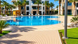 A swimming pool with lounge chairs, palm trees, and a modern building with balconies. - Luxury Apartment in Agadir Bay, Swimming Pools and Large Terrace 5 Minutes from the Beach (Agadir)