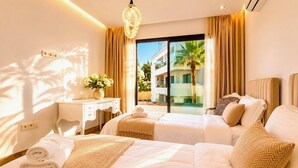 A hotel room with two beds, a desk, and a view of a building and palm trees. - Luxury Apartment in Agadir Bay, Swimming Pools and Large Terrace 5 Minutes from the Beach (Agadir)