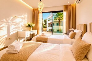 A hotel room with two beds, a desk, and a view of a building and palm trees. - Luxury Apartment in Agadir Bay, Swimming Pools and Large Terrace 5 Minutes from the Beach (Agadir)