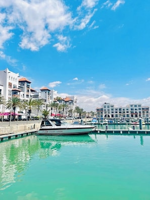 A marina with a white boat named 'GALAXY LOISIRS' docked, surrounded by multi-story buildings with balconies and palm trees. - Luxury Apartment in Agadir Bay, Swimming Pools and Large Terrace 5 Minutes from the Beach (Agadir)