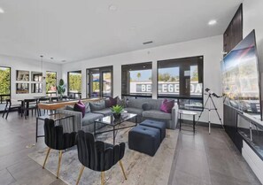 Ein modernes Wohnzimmer mit Sofa, Couchtisch und Sesseln, großen Fenstern und Blick ins Freie.