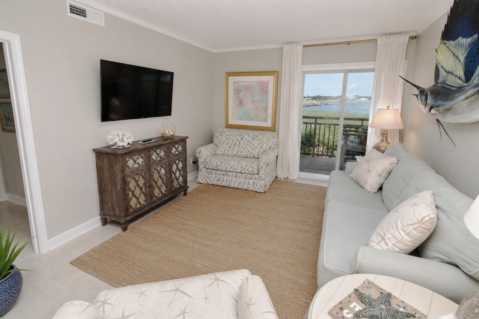 A living room with a sofa, a television, a cabinet, and a view of the outdoors.