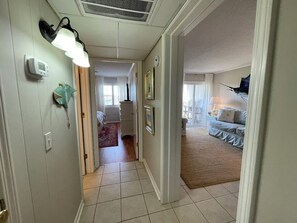A hallway with a light fixture, a thermostat, and a door leading to a bedroom with a bed and a nightstand. - Inlet Pointe 23 - Second Row (Channelfront) in Garden City Beach (Garden City Beach)