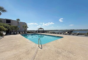 Ein Swimmingpool mit Liegestühlen und einer Laube, umgeben von einem Zaun und Palmen.